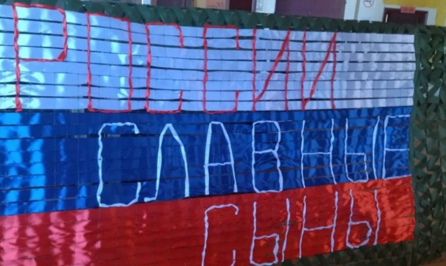 Это пункт плетения маскировочных сетей села Половинное. Вот так волонтеры из лент своими руками сплели флаг России, который стал символом их работы